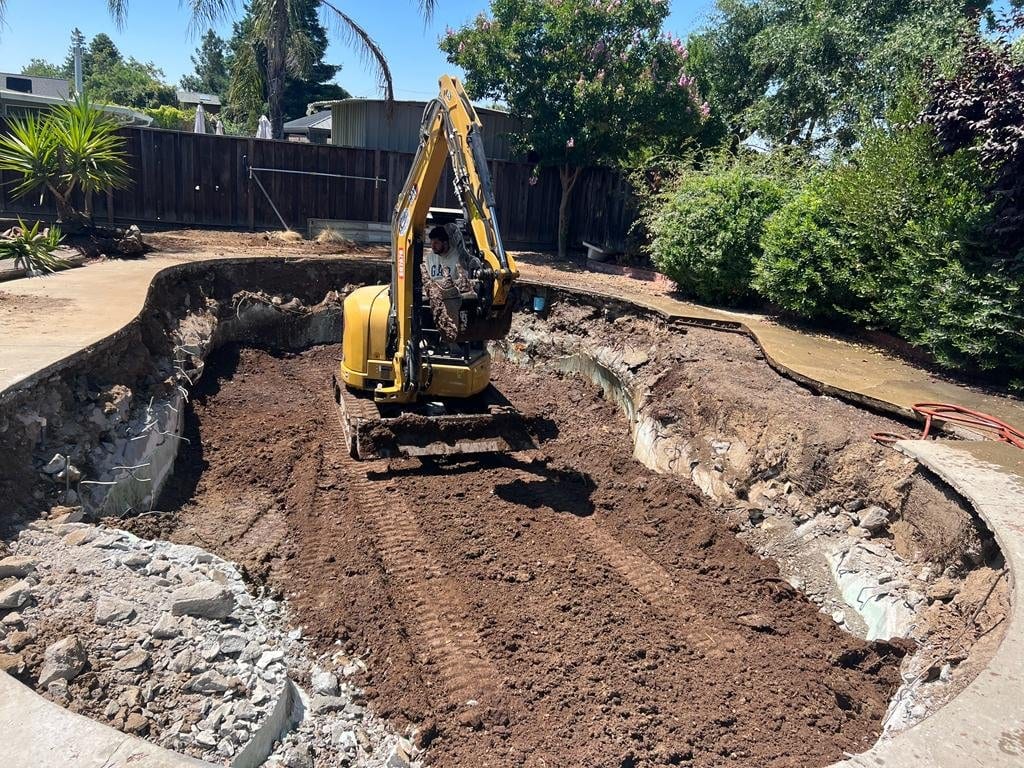 Excavator demolishing an in-ground swimming pool in a Bay Area backyard
